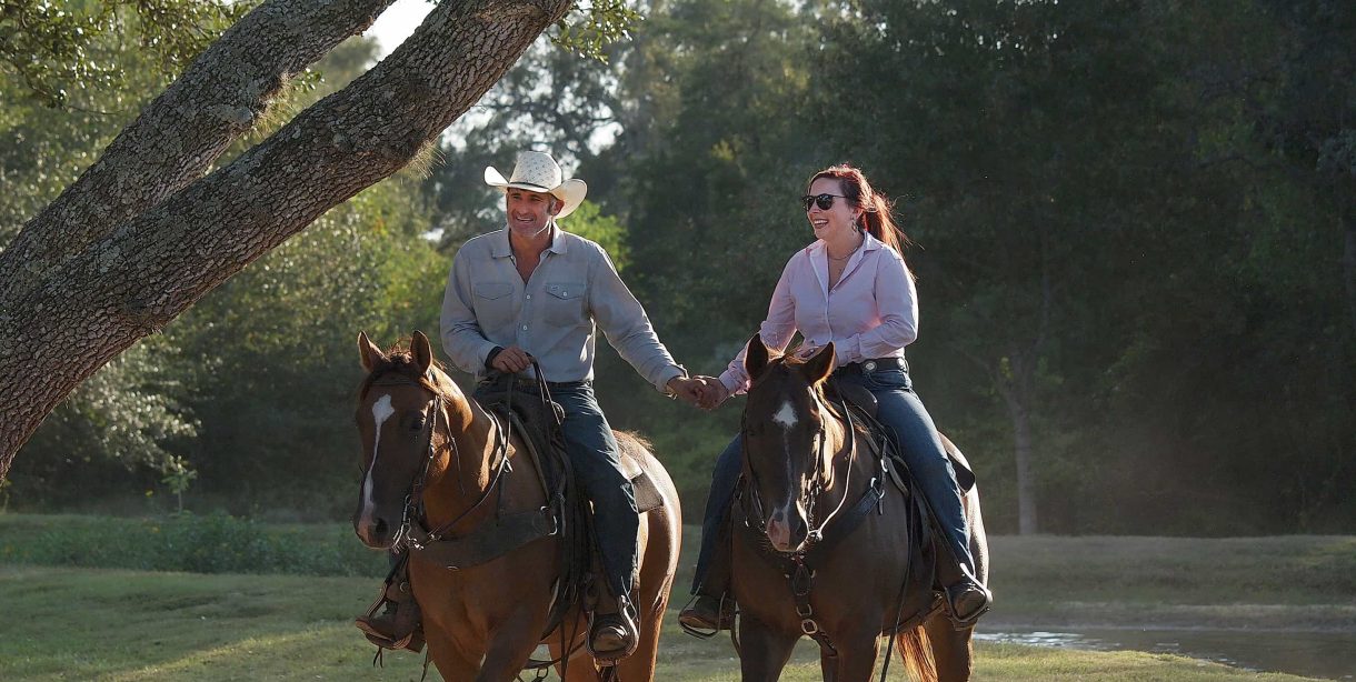 Couple holding hands on horseback at BlissWood Ranch